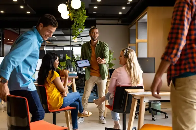 Business man presenting in front of a diverse group of colleagues using a tablet