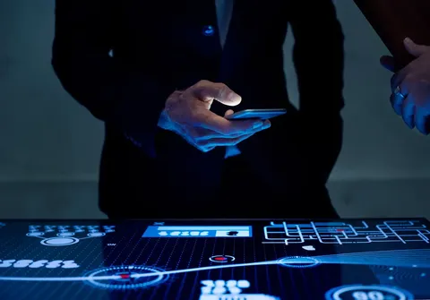 A man holding a cellphone next to a futuristic hologram desk
